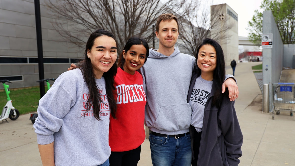 Four students with arms around each other standing outside near Cunz Hall