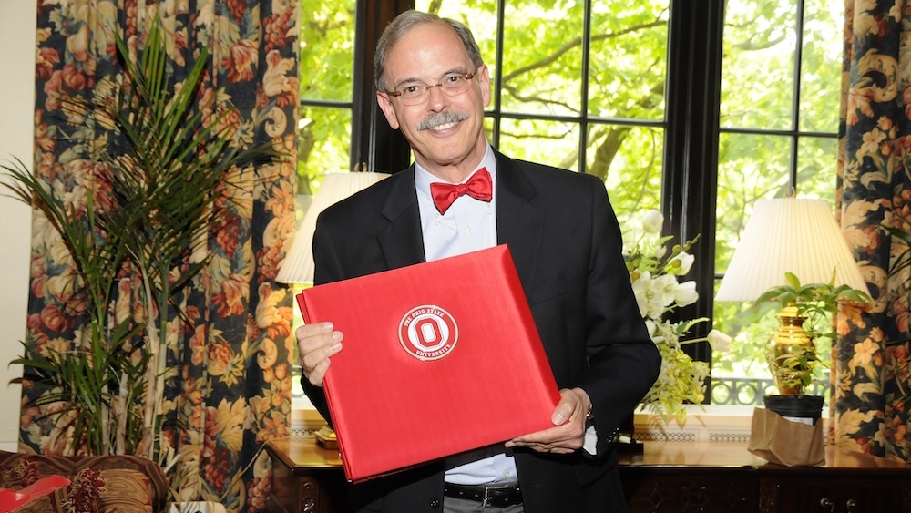 Jeff Caswell stands in an office holding a diploma