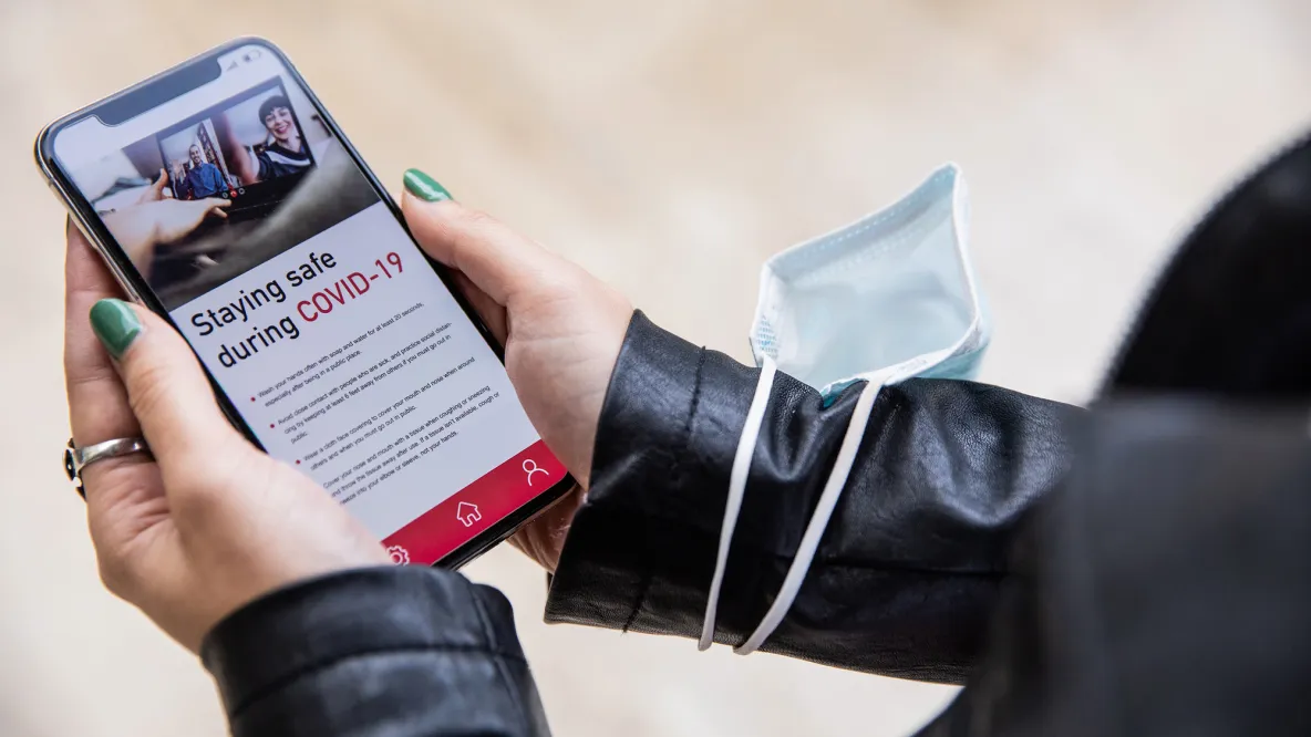 A person holds a phone, displaying a news article about staying safe during COVID-19.