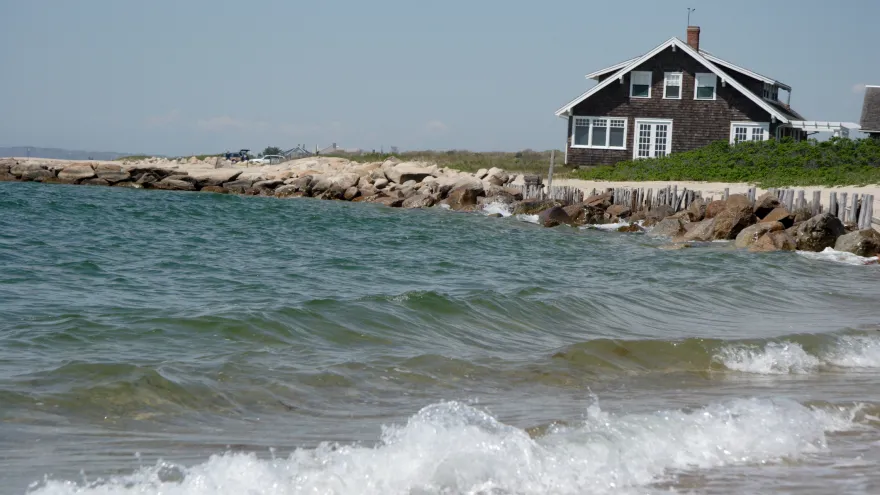 A small gray and white house on the edge of the seashore