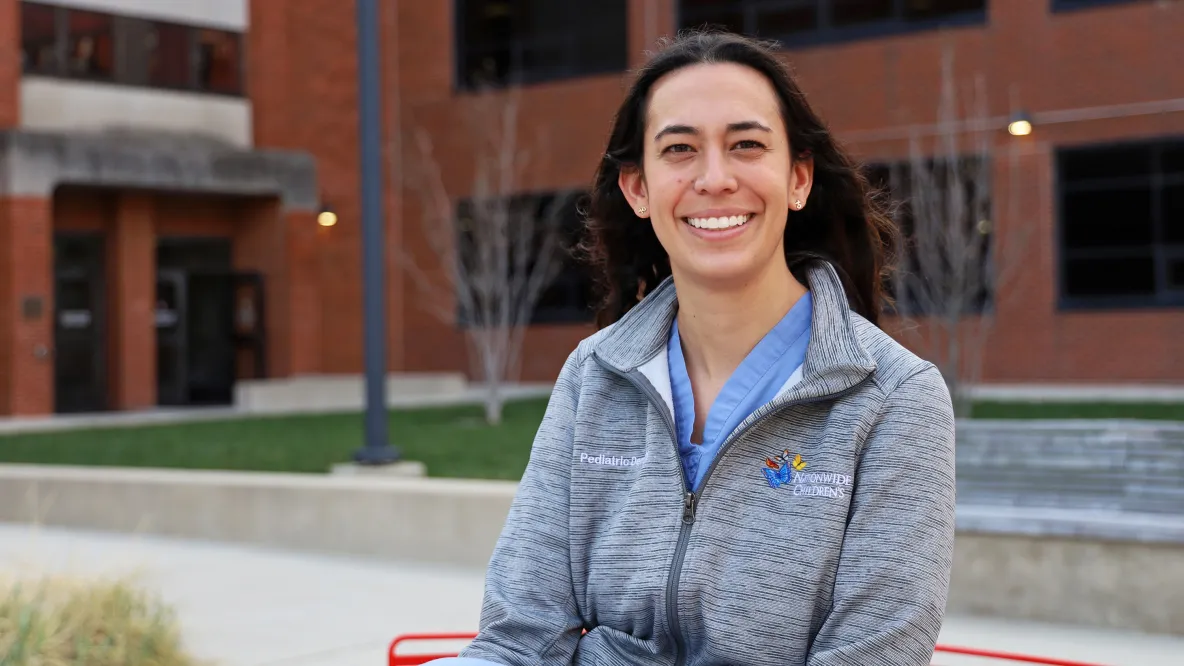 A woman in a gray zip up sweater smiles outside