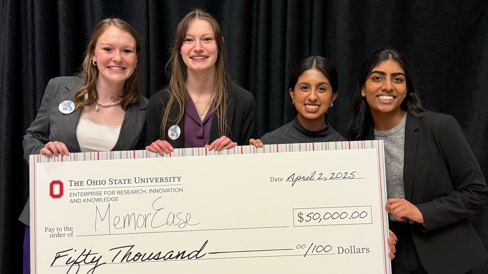 Four students smiling pose with a large check written out to MemorEase