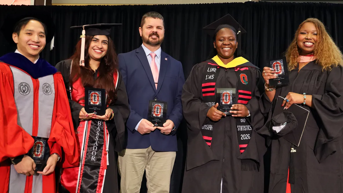 five students stand in a row smiling and holding awards.