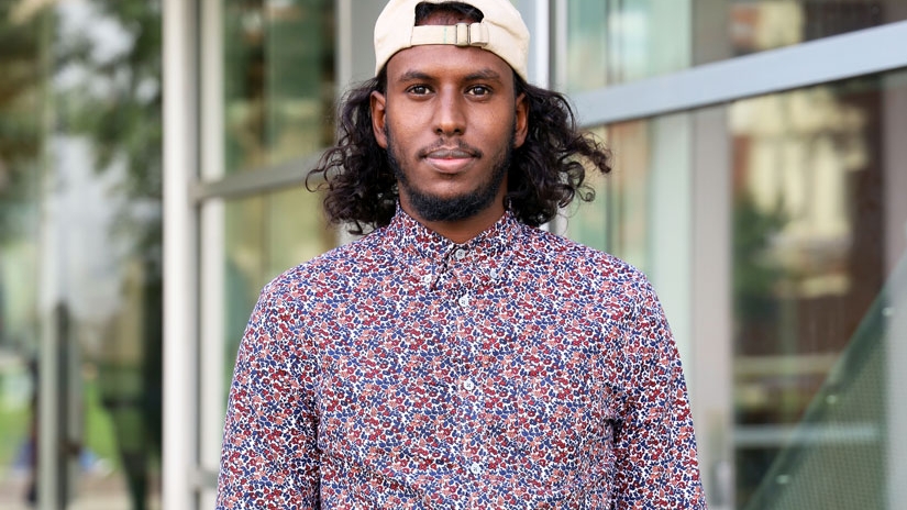 Sharmake standing in front of Cunz Hall wearing baseball hat backwards