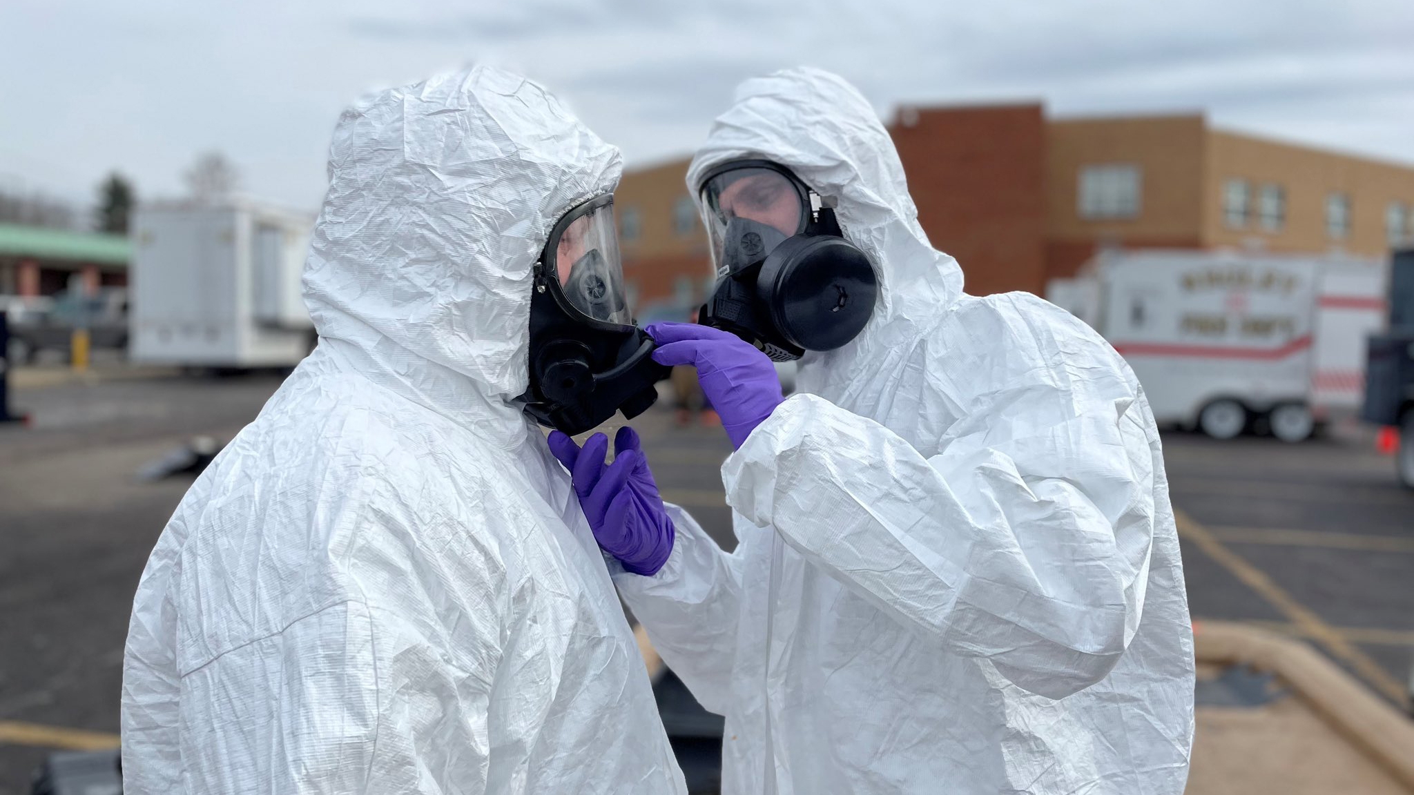 two people in white personal protective equipment and purple gloves.