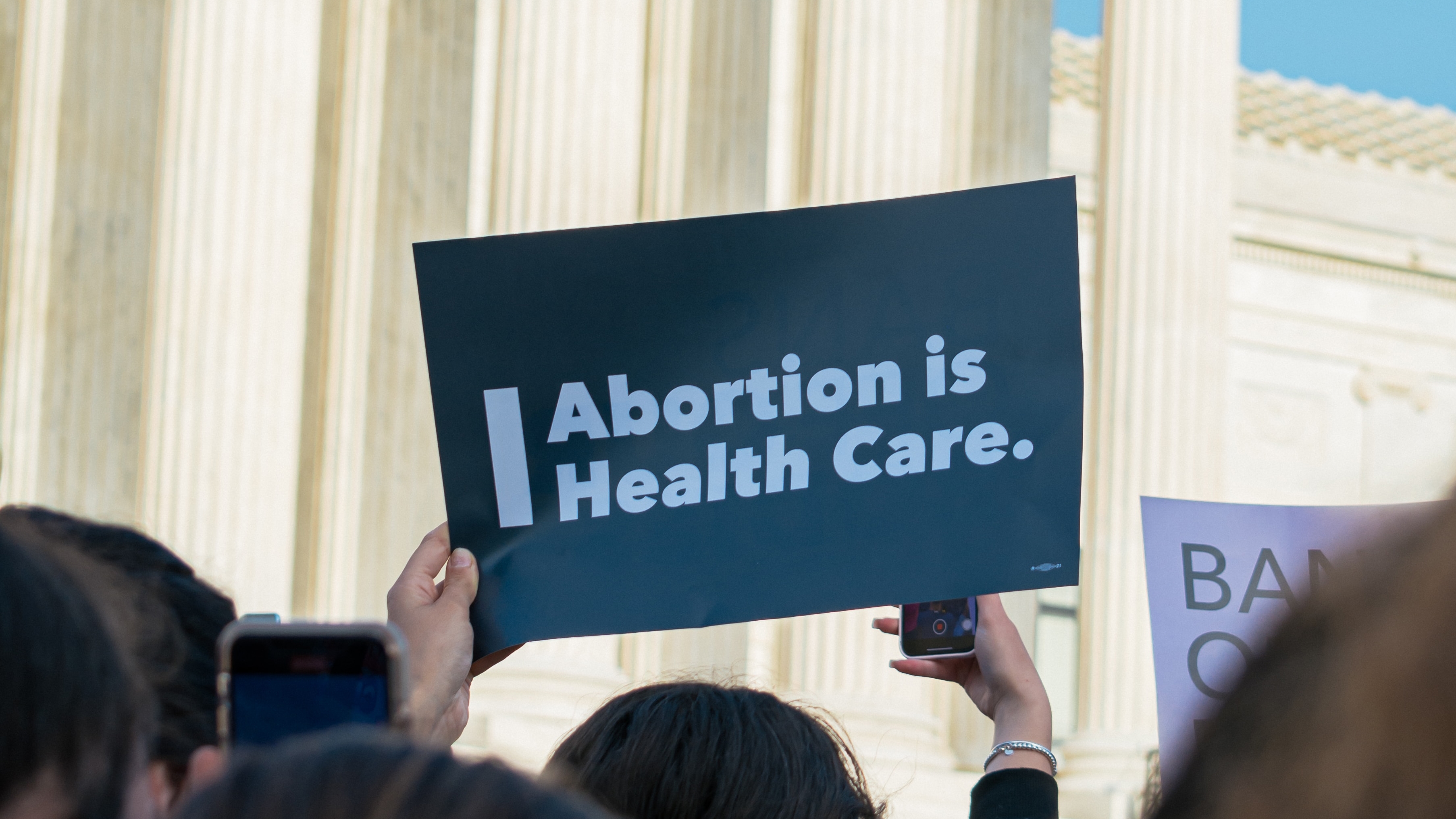 person holding a sign reading "abortion is health care" in front of the U.S. Supreme Court