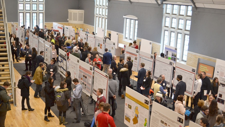 A busy room of people presenting and listening to research results during a poster session