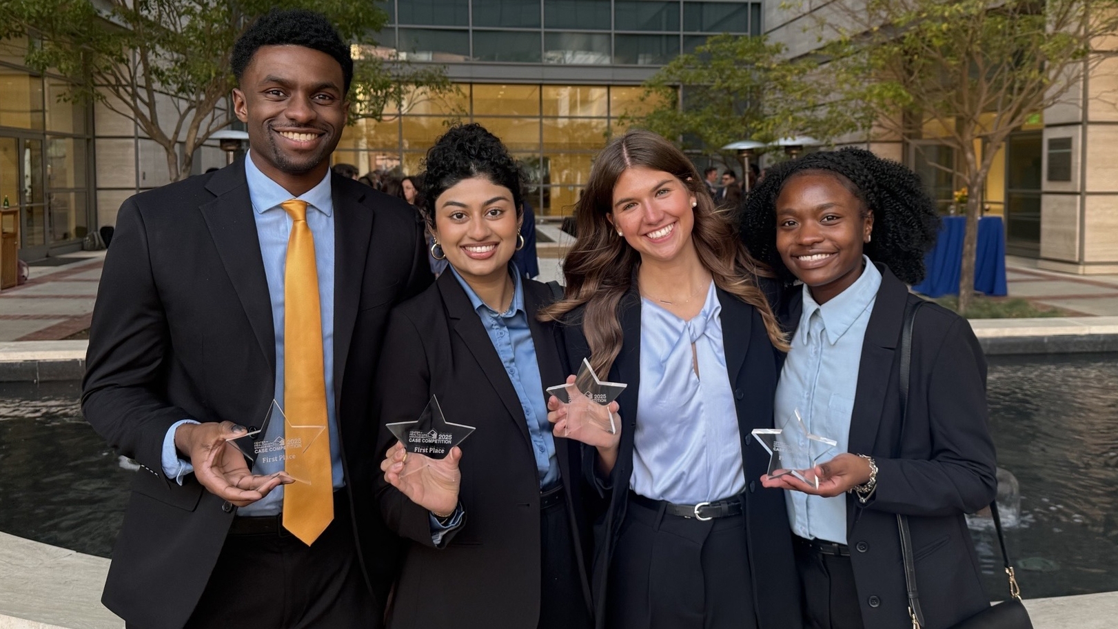 Four students dressed in professional clothes pose for a photo holding awards in Los Angeles.