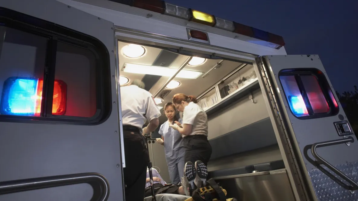 an ambulance at night wiht hte doors open and a patient and caregivers inside