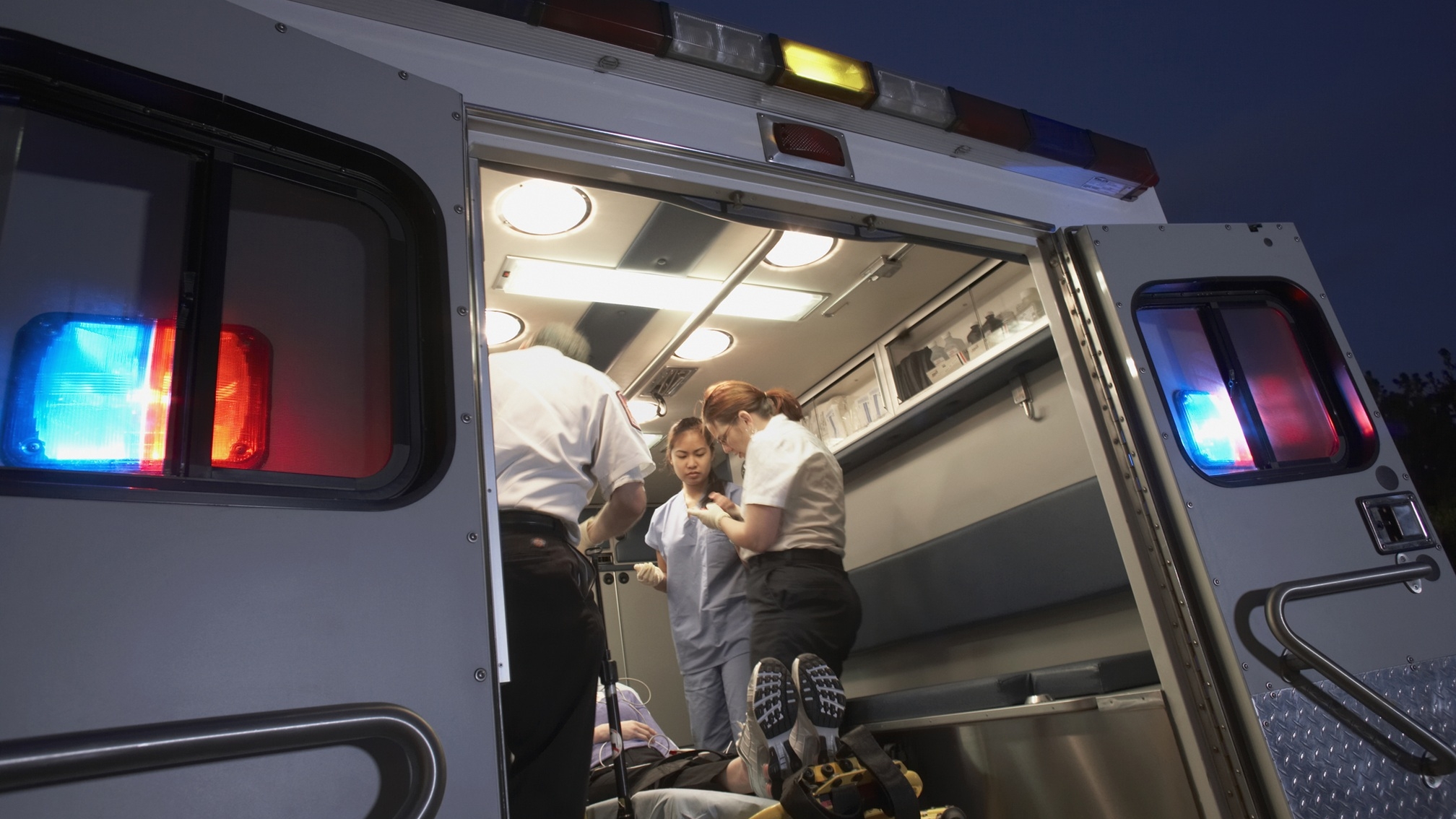 an ambulance at night wiht hte doors open and a patient and caregivers inside