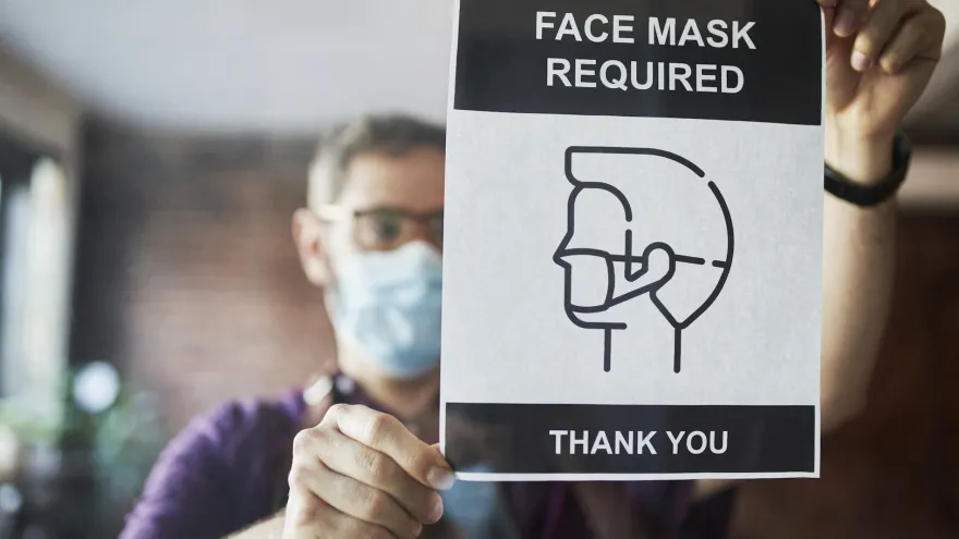 Man posting a sign that says masks are required