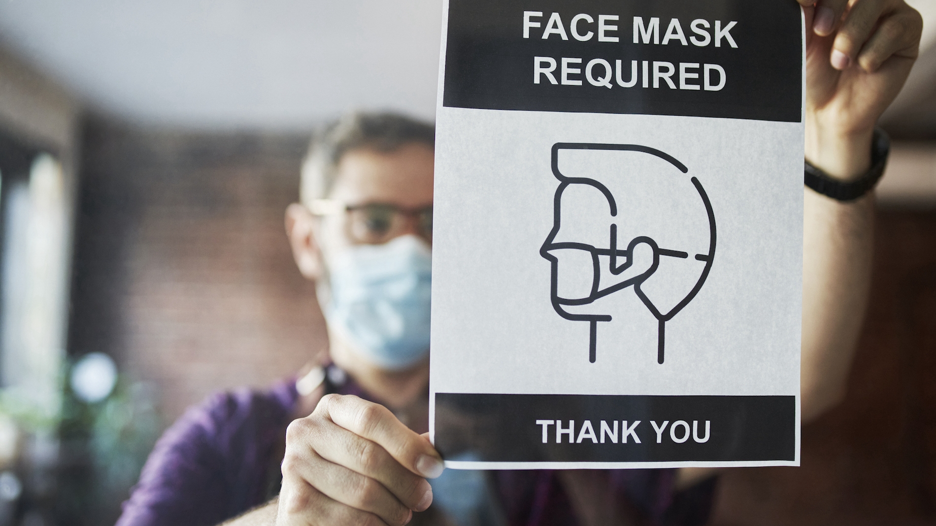 Man posting a sign that says masks are required