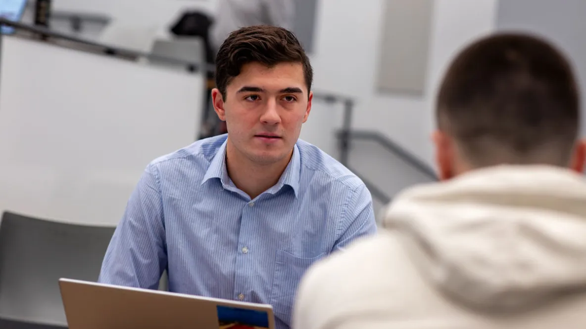 Man in blue shirt talks to another across a table