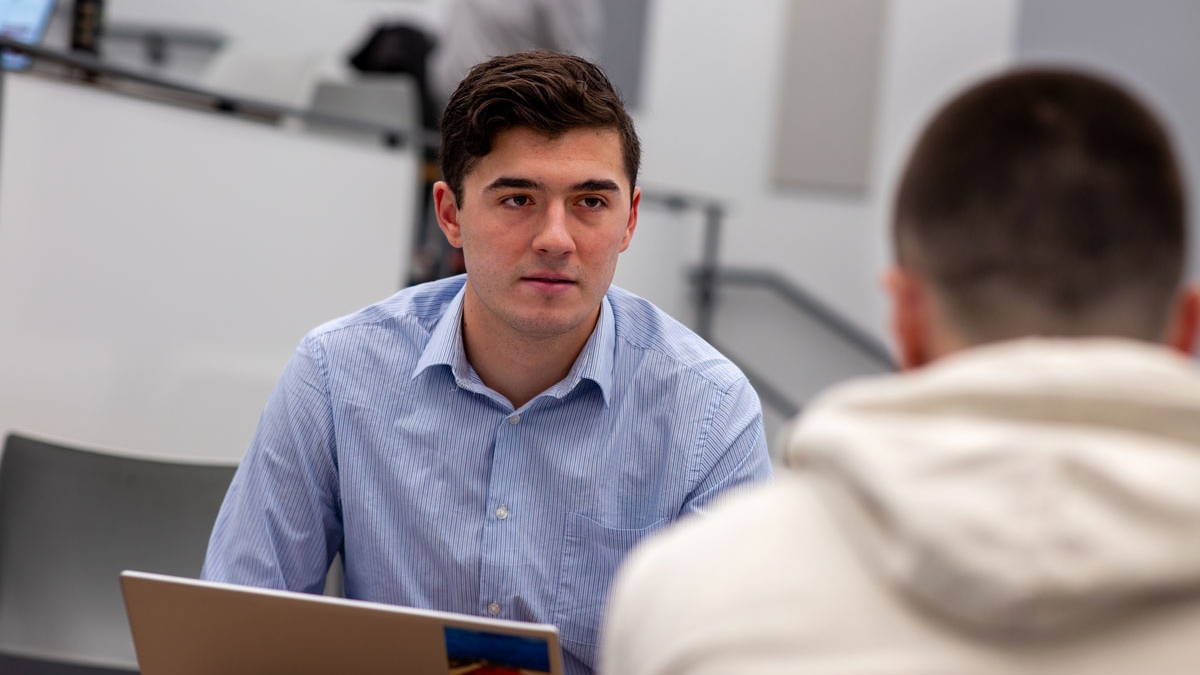 Man in blue shirt talks to another across a table