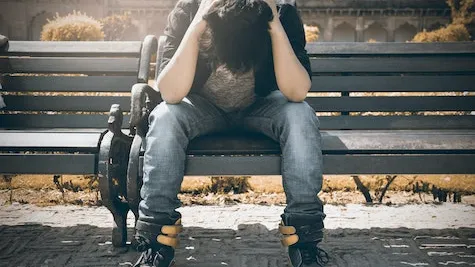 person sitting on bench holding their head in their hands