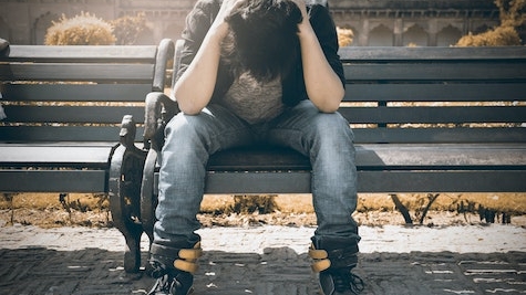 person sitting on bench holding their head in their hands
