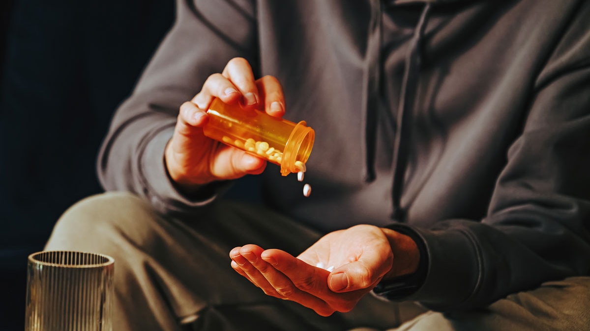 Person in a dark gray hooded sweatshirt pours pills from a bottle into their hand