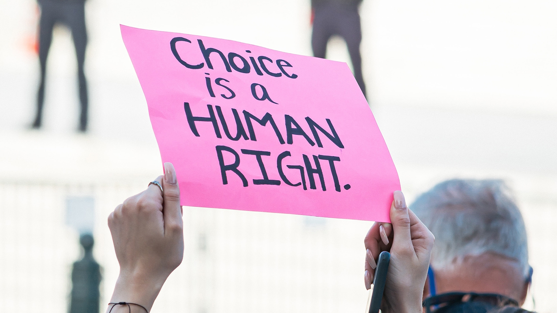 a person raising their arms with a pink sign that reads Choice is a human right.