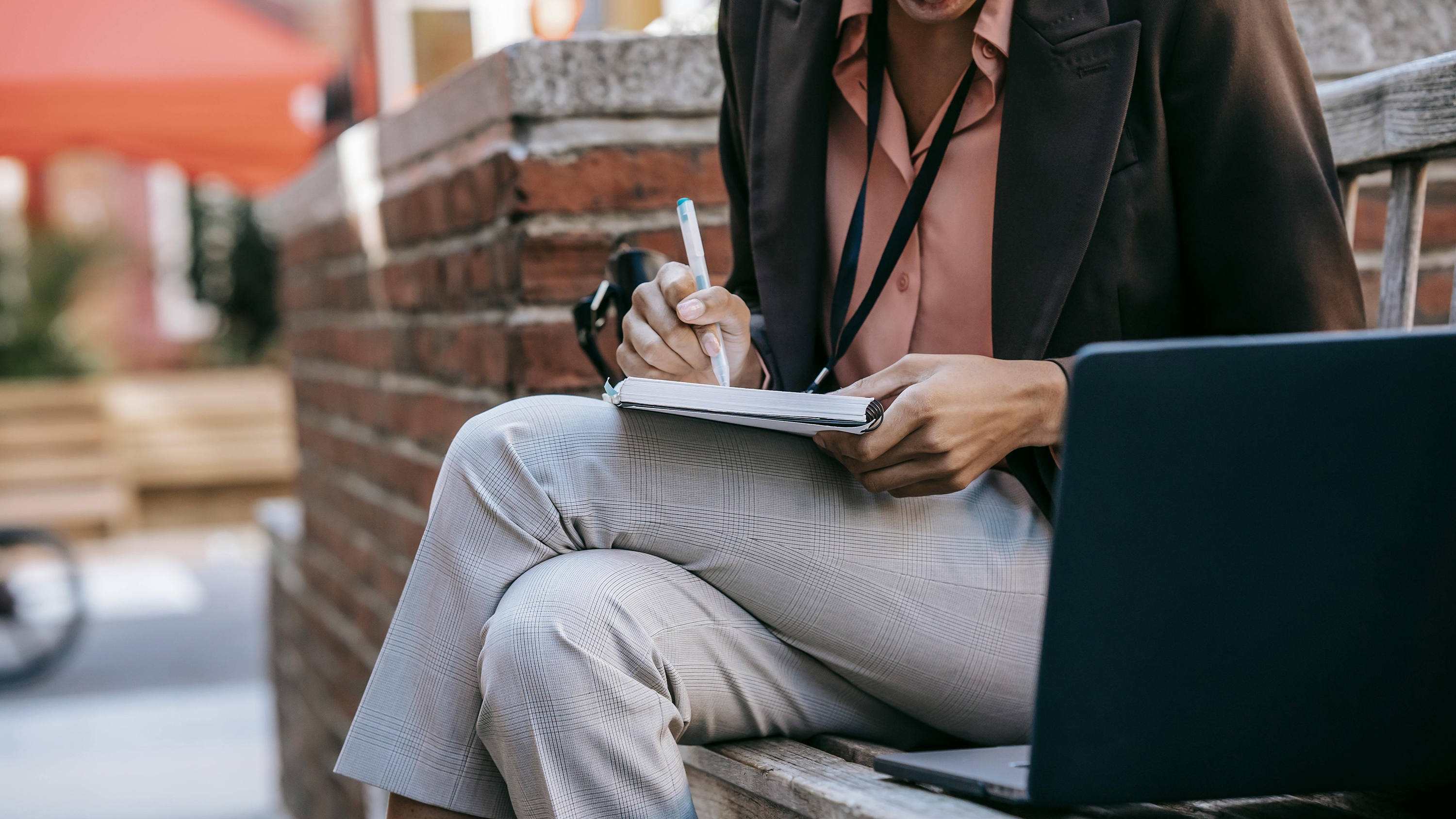 person writing in a notebook in front of a laptop