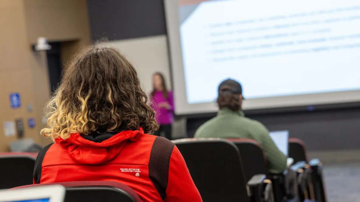 A view from behind of a student sitting in a classroom auditorium for a lecture