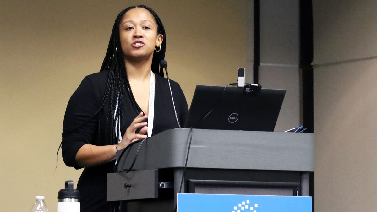 Woman stands at podium with a computer sharing her presentation at a conference
