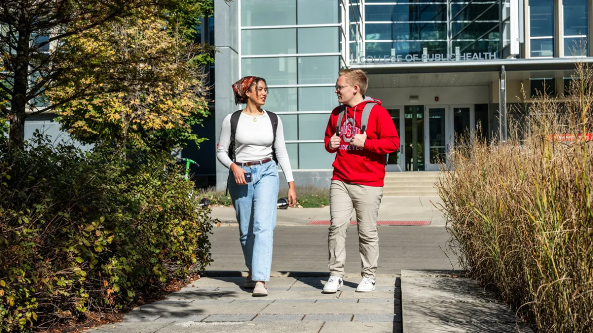 Two public health students walk down a path along the water garden at Cunz Hall