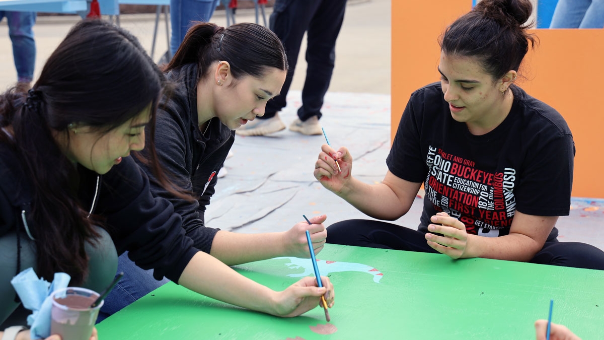 Three public health students decorate a playhouse built for a local family