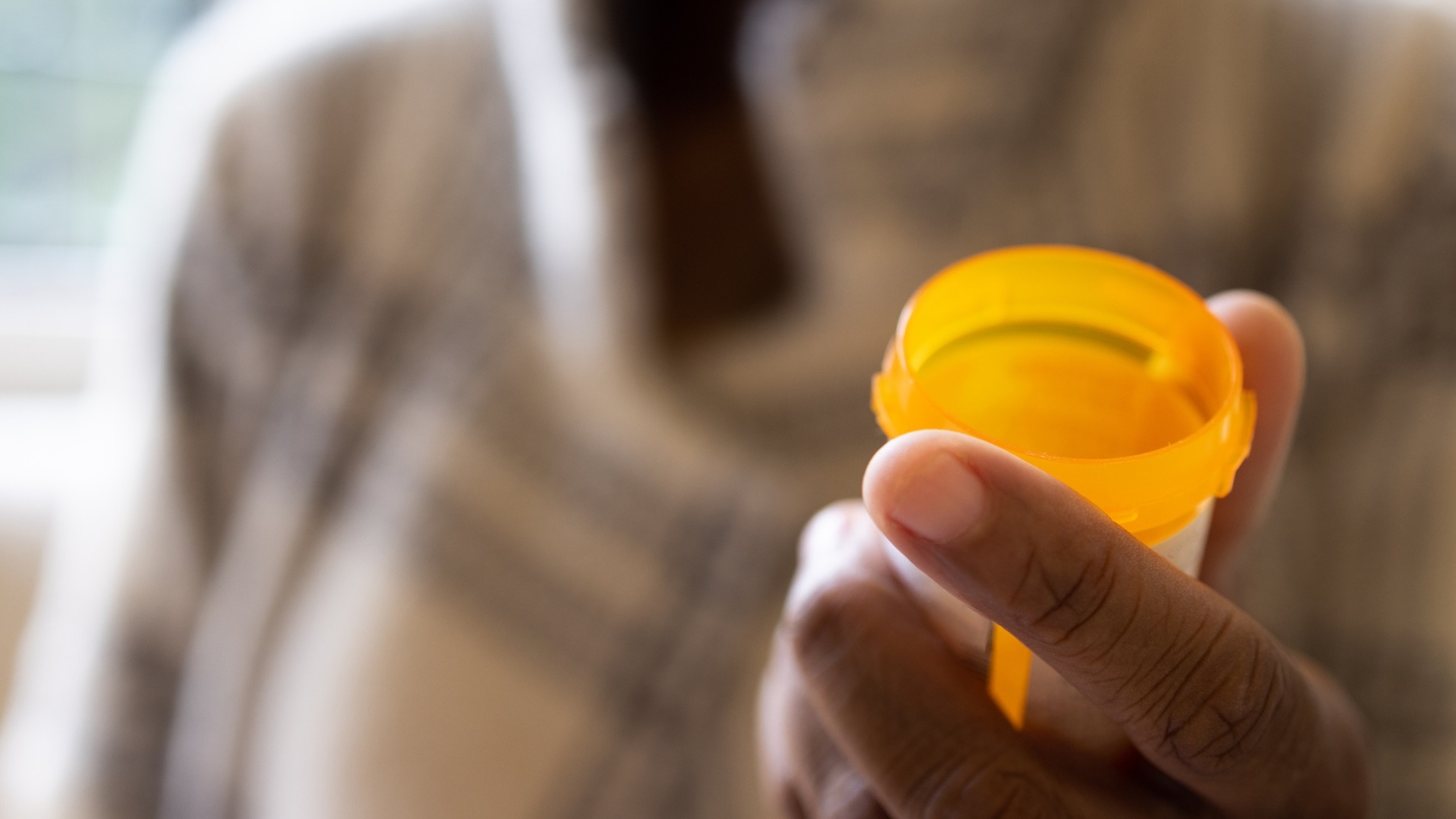 Man's hand in foreground holding empty prescription bottle