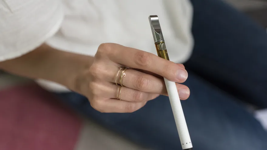 A young woman's hand, holding a vaping device
