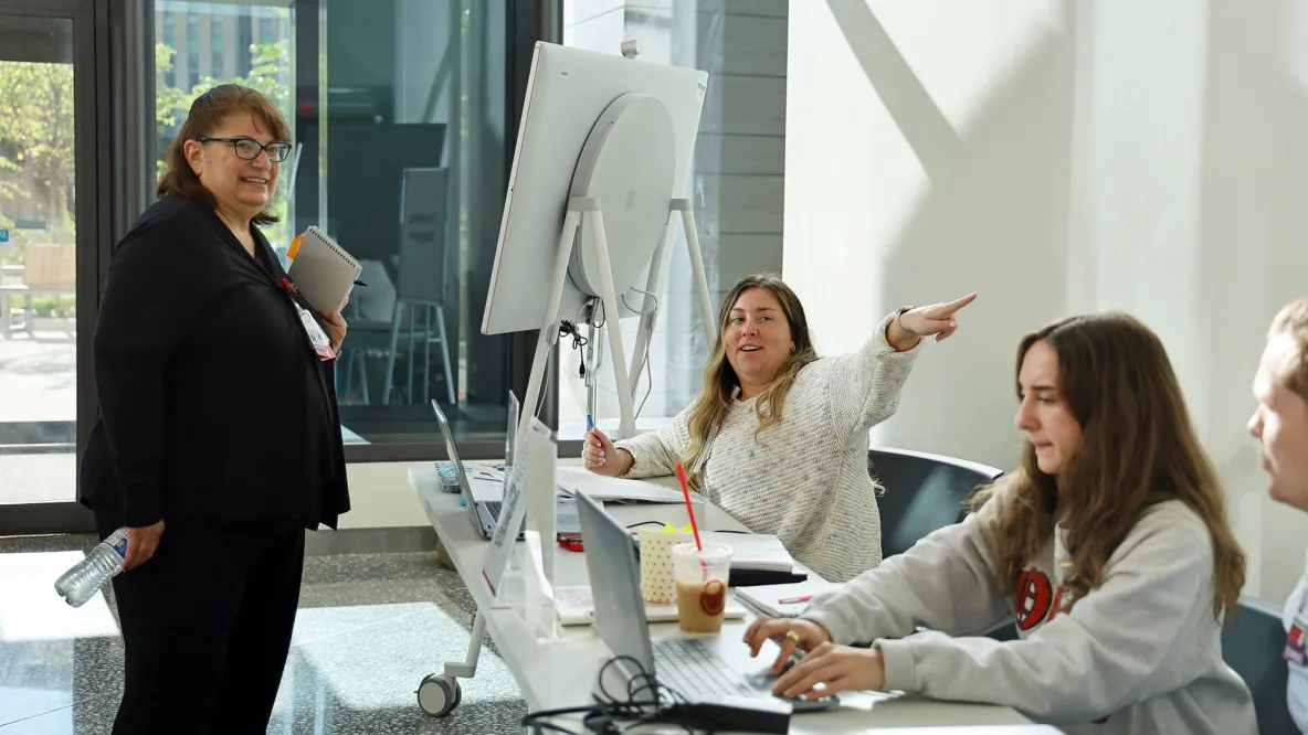 A student provides directions to a hospital employee while another student types on a laptop