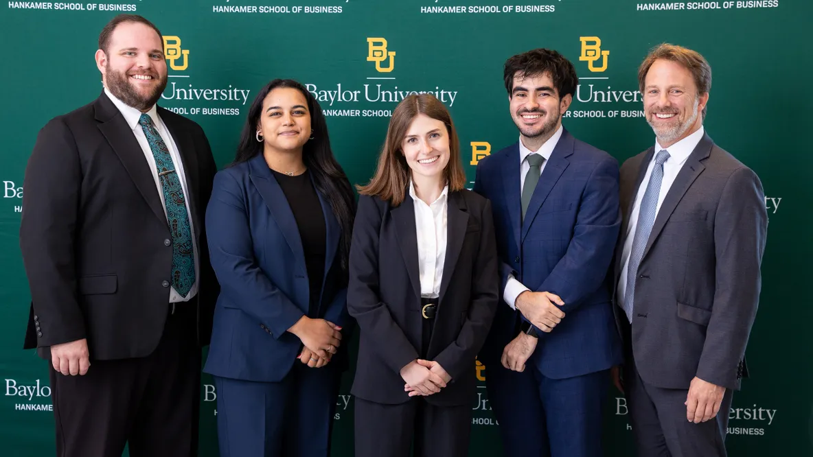 five people in business attire stand in front of a green background that says "Baylor University."