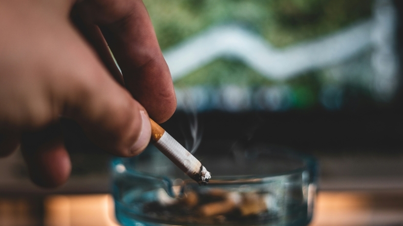 a person holds a cigarette over an ash tray.