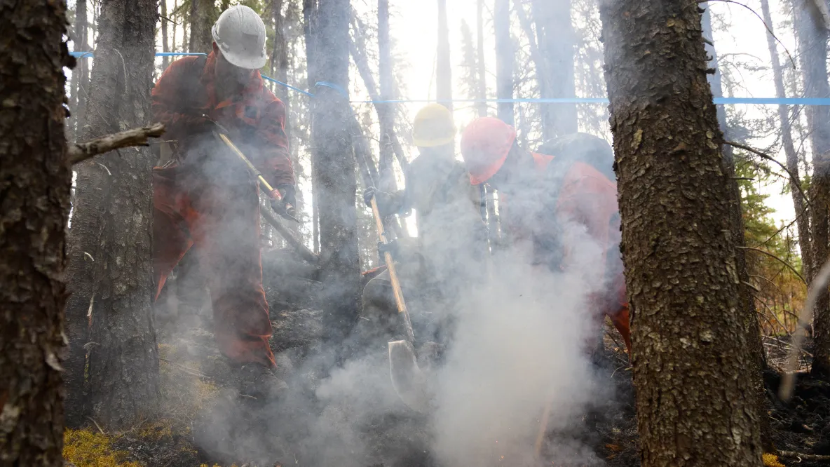 Three people holding shovels are outside in smokey conditions.
