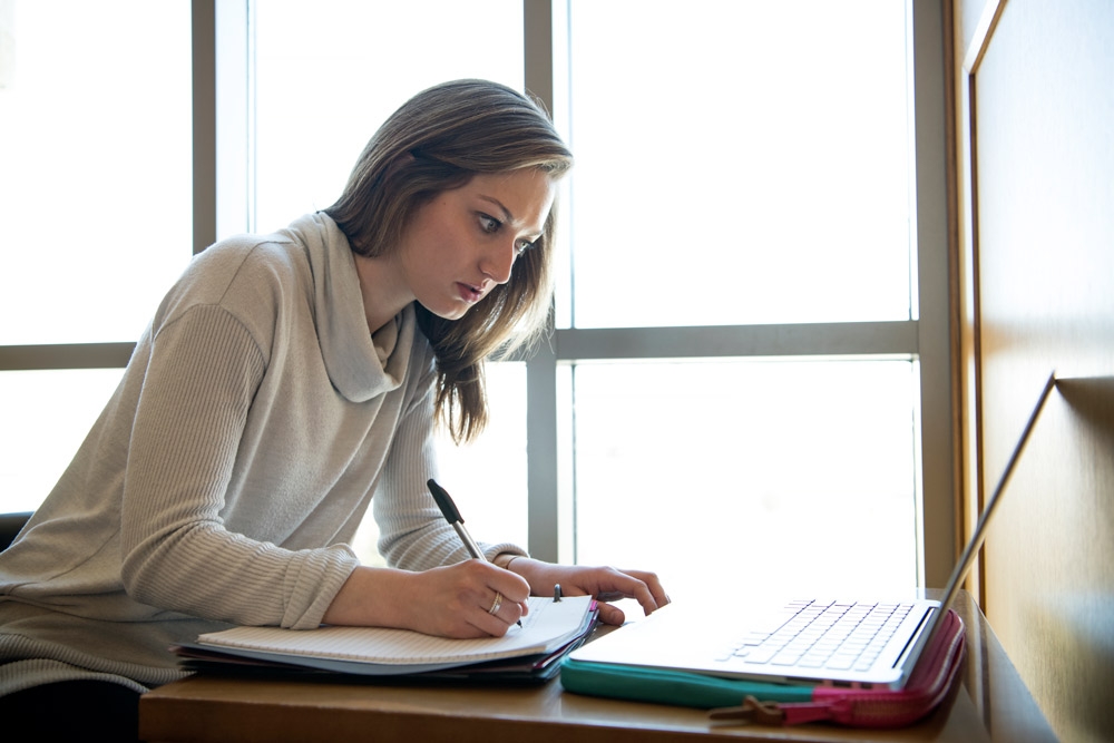 Student writing notes and looking at computer