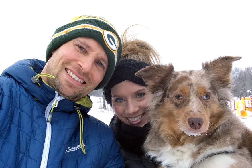 two people dressed in winter cloths pose with a brown and white dog