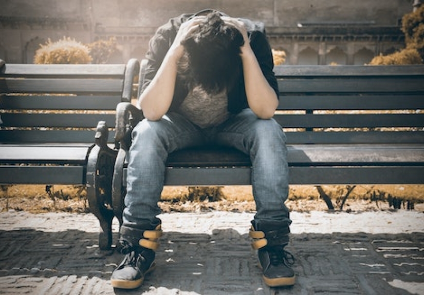 person sitting on bench holding their head in their hands