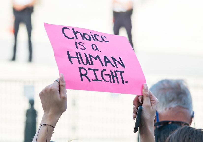 a person raising their arms with a pink sign that reads Choice is a human right.