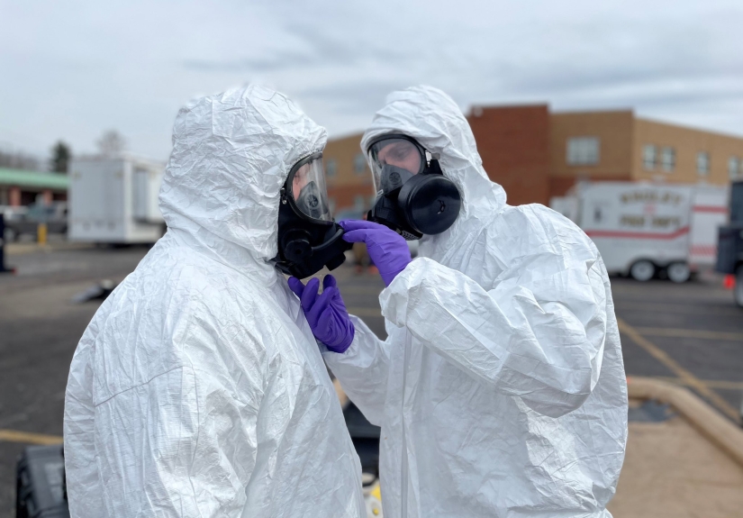 two people in white personal protective equipment and purple gloves.
