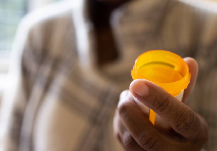 Man's hand in foreground holding empty prescription bottle