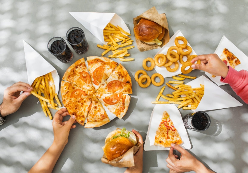 Hands reaching toward a table of foods including pizza, onion rings and burgers