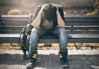 person sitting on bench holding their head in their hands
