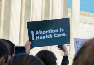 Image of someone holding a sign reading "abortion is health care" in front of the U.S. Supreme Court.